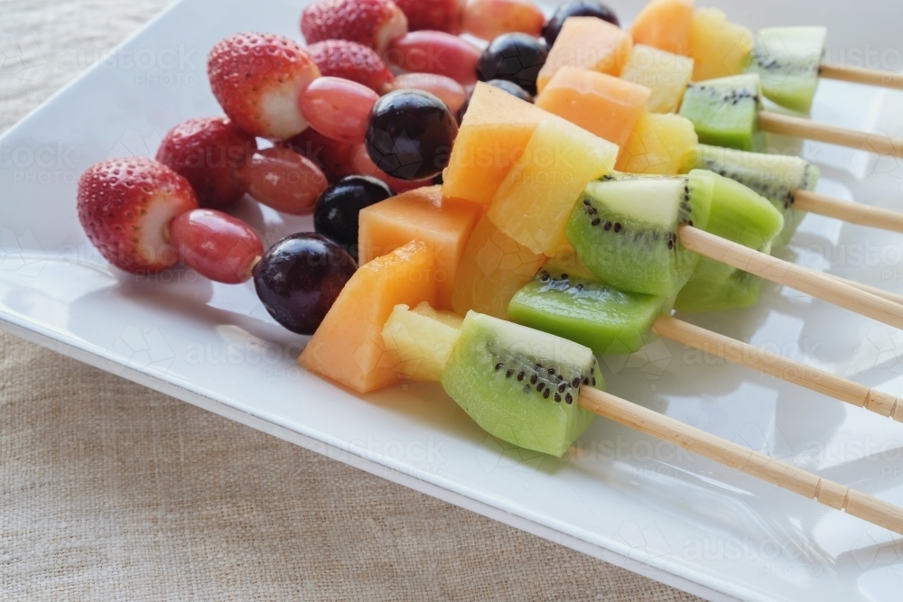 Fresh rainbow fruit skewers on white plate - Australian Stock Image