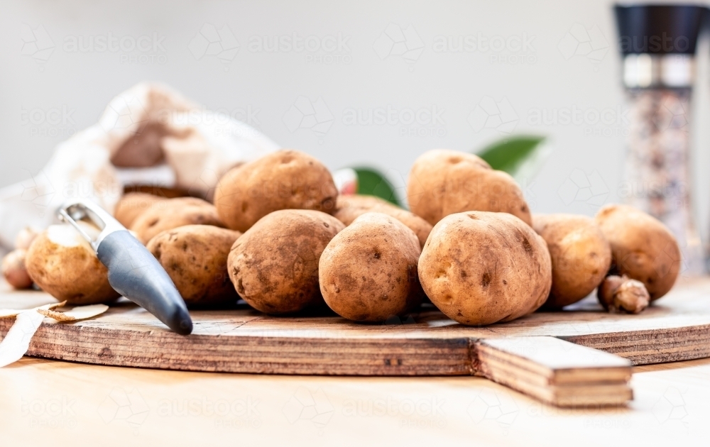Fresh unpeeled potatoes on a chopping board with a shallow depth of field - Australian Stock Image