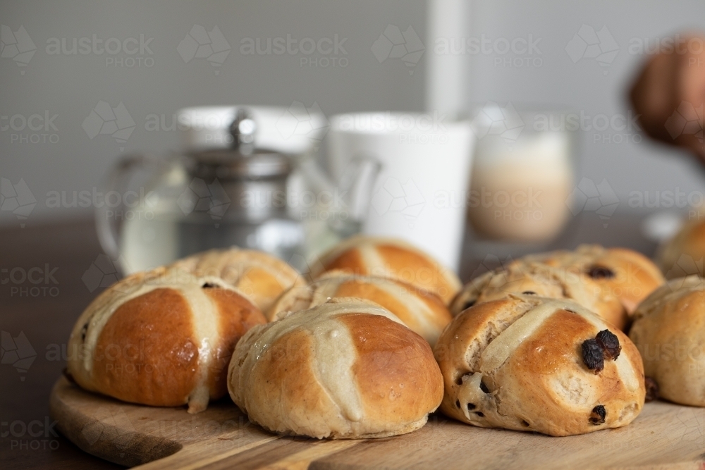 freshly made hot cross buns on table with teapot and cups - Australian Stock Image