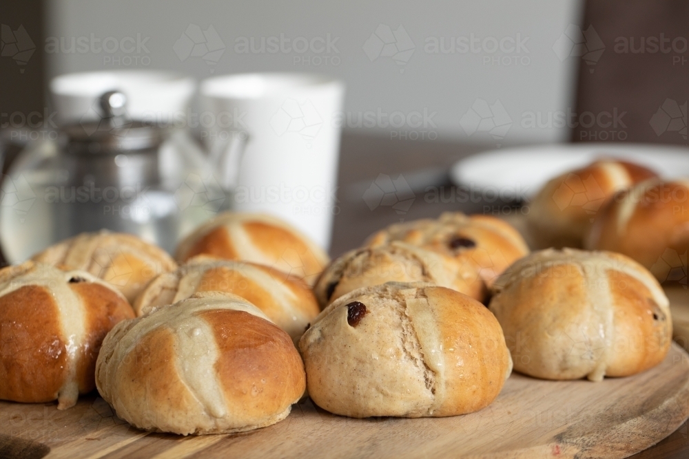 freshly made hot cross buns on table with teapot and cups - Australian Stock Image