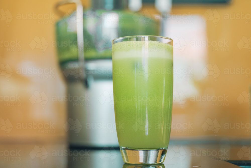 Freshly squeezed green juice with juicing machine in background - Australian Stock Image