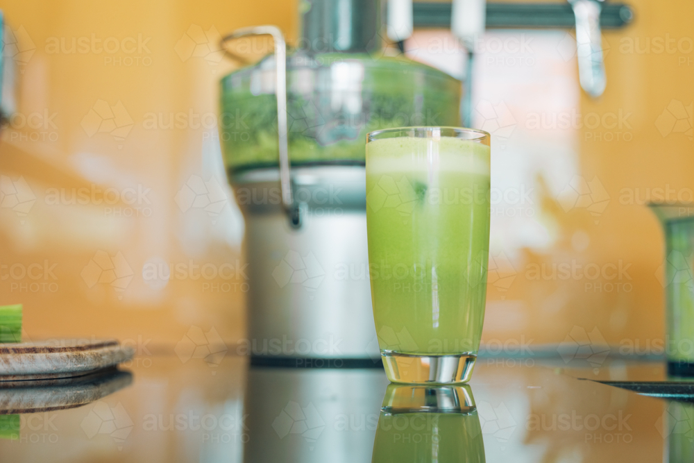 Freshly squeezed green juice with juicing machine in background - Australian Stock Image