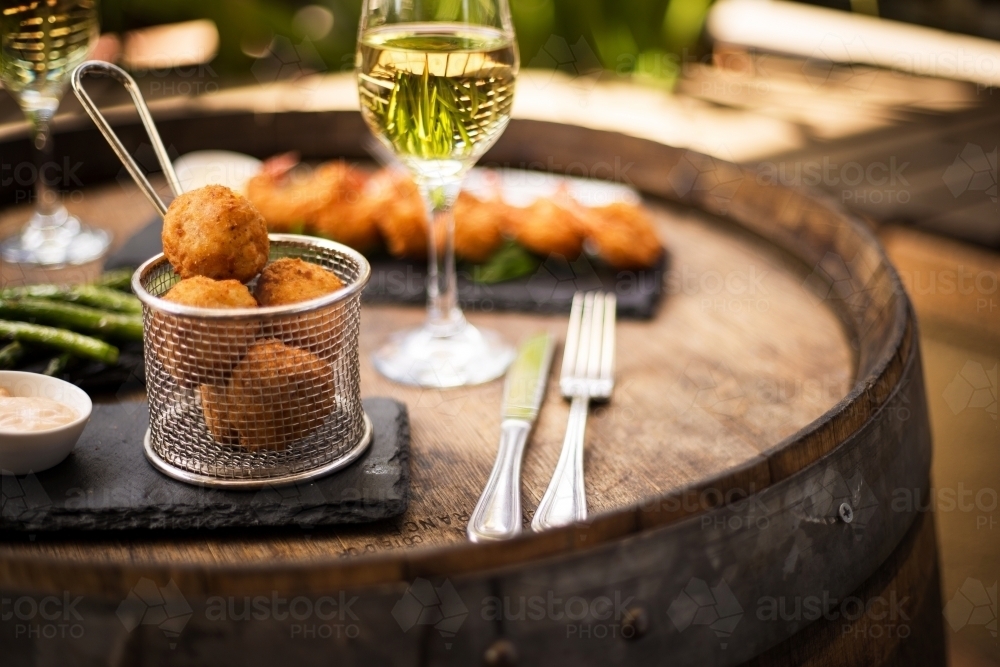 Fried cheese balls served in metal basket on a black plate with cream sauce and utensils on the side - Australian Stock Image