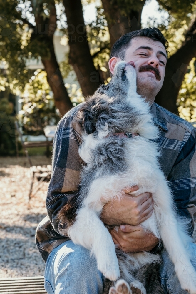 Friendly dog licking mans face. - Australian Stock Image