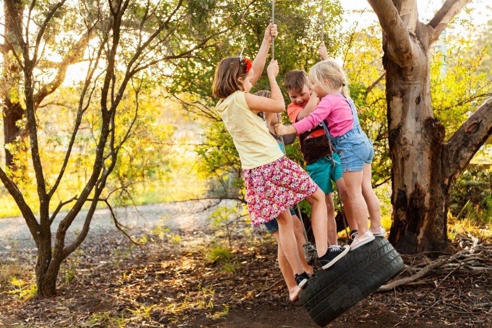 Friends playing together on tyre swing - Australian Stock Image