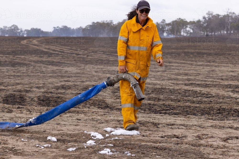 Front view of woman firefighter holding hose in burnt paddock - Australian Stock Image