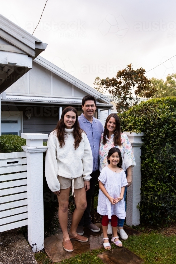Full body portrait of a happy family posing in front of a white house - Australian Stock Image