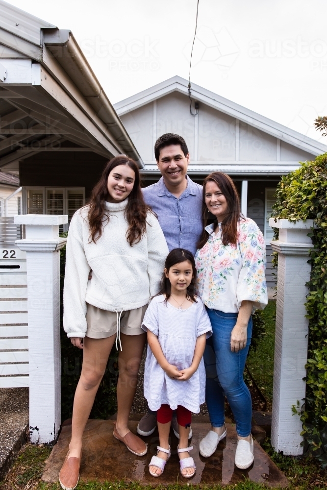 Full body portrait of a happy family posing in front of a white suburban house - Australian Stock Image