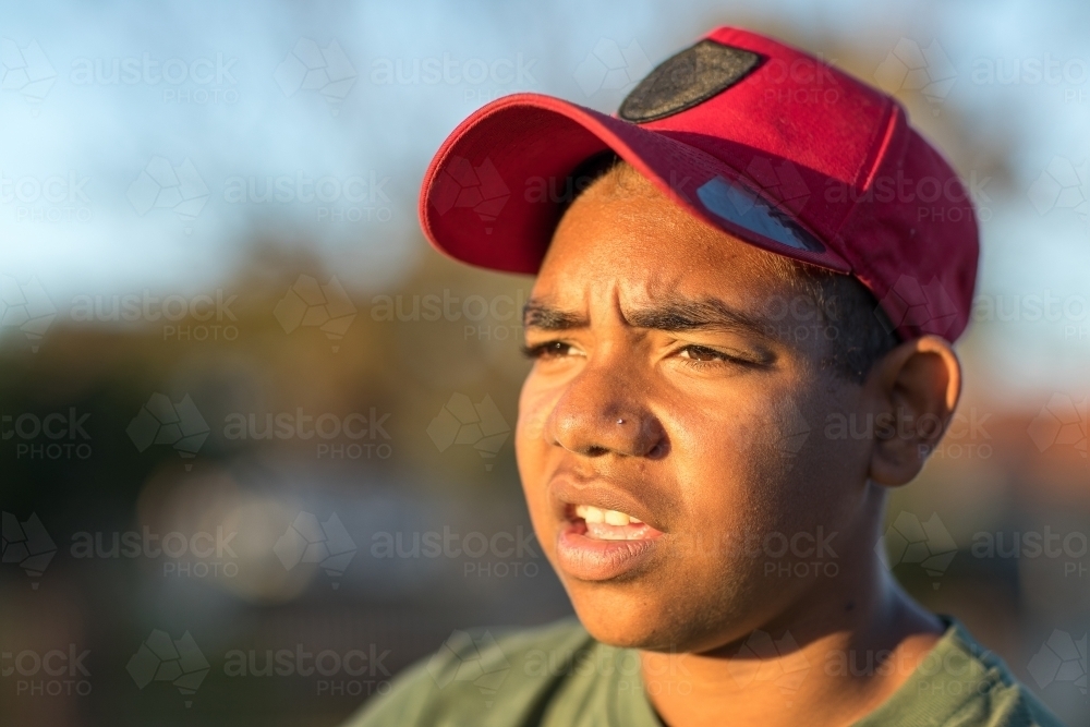 full face view of teen boy with furrowed brow wearing red baseball cap - Australian Stock Image