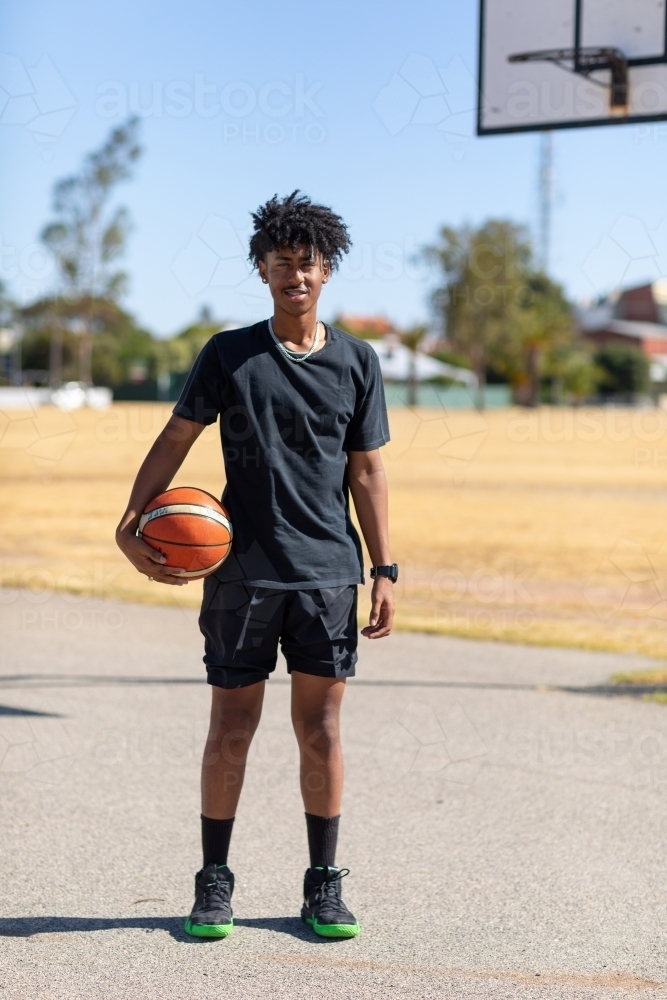 full length basketball player standing looking at camera with basketball - Australian Stock Image