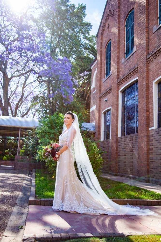 Full length shot of smiling bride with flowing veil outside a church - Australian Stock Image