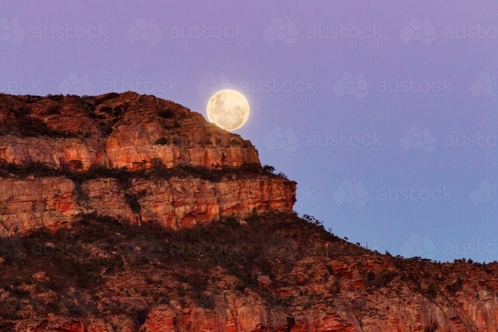 Full moon rising behind rocky hill - Australian Stock Image