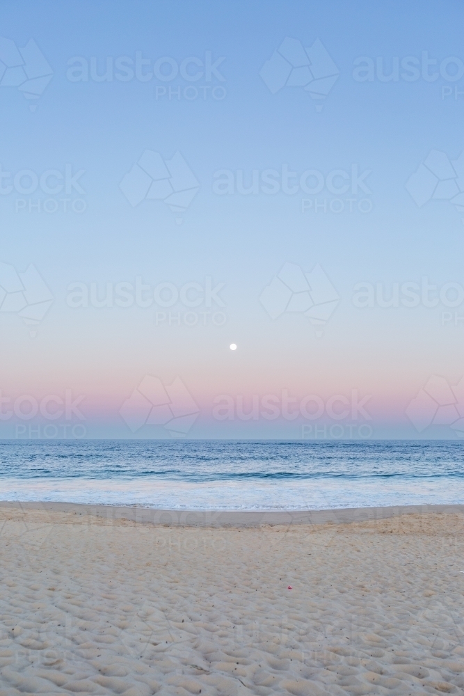 Full moon rising in dusk light over ocean and sandy seashore  - Australian Stock Image