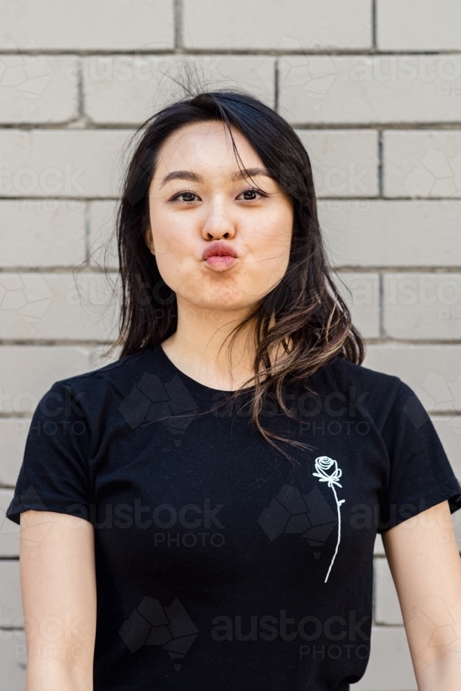 funny portrait of asian woman against a brick wall - Australian Stock Image