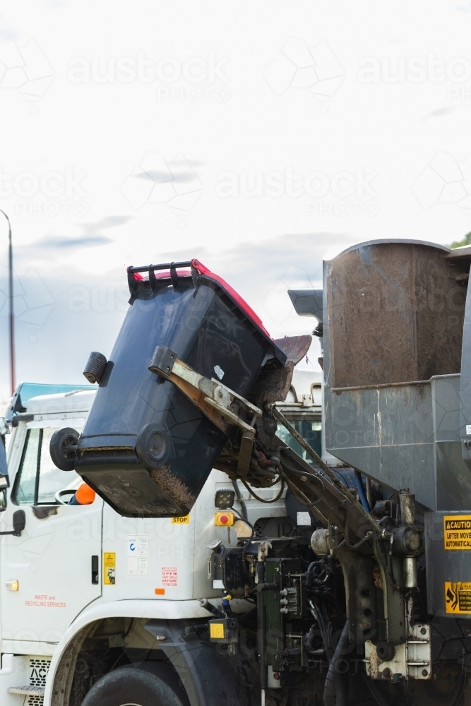 Garbage truck collecting red bin household waste in suburban area of town - Australian Stock Image