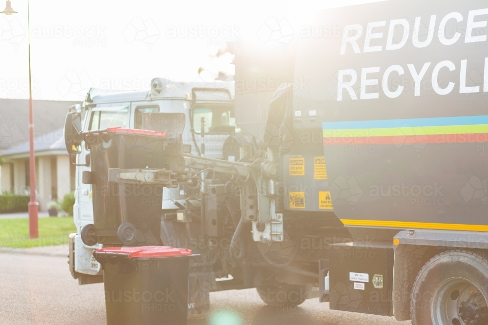 Garbage truck picking up bins from curb side in suburban area - Australian Stock Image