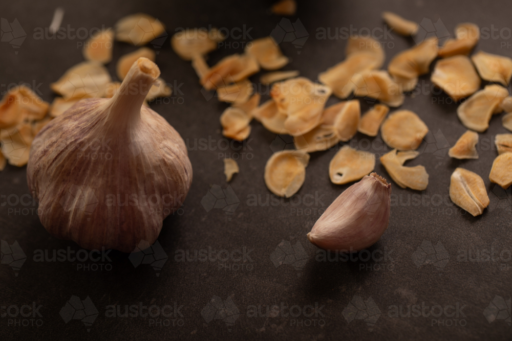 Garlic bulb with clove and garlic chips on dark benchtop - Australian Stock Image
