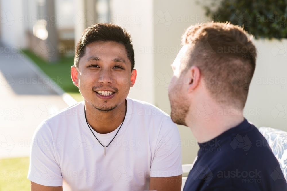 Gay couple sitting outside, mixed race - Australian Stock Image