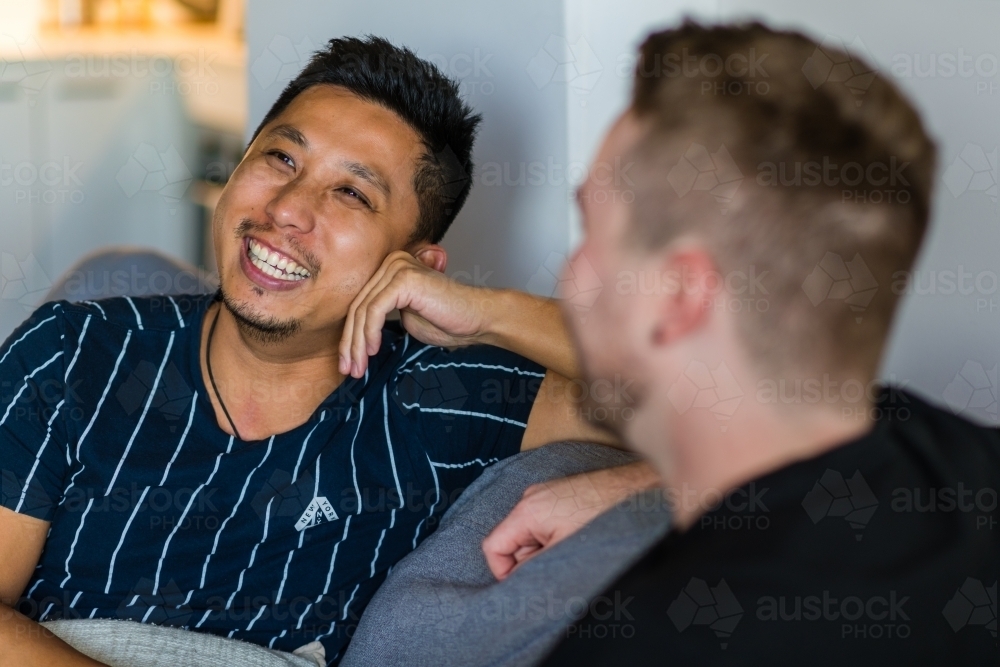 Gay couple talking and laughing on the couch - Australian Stock Image