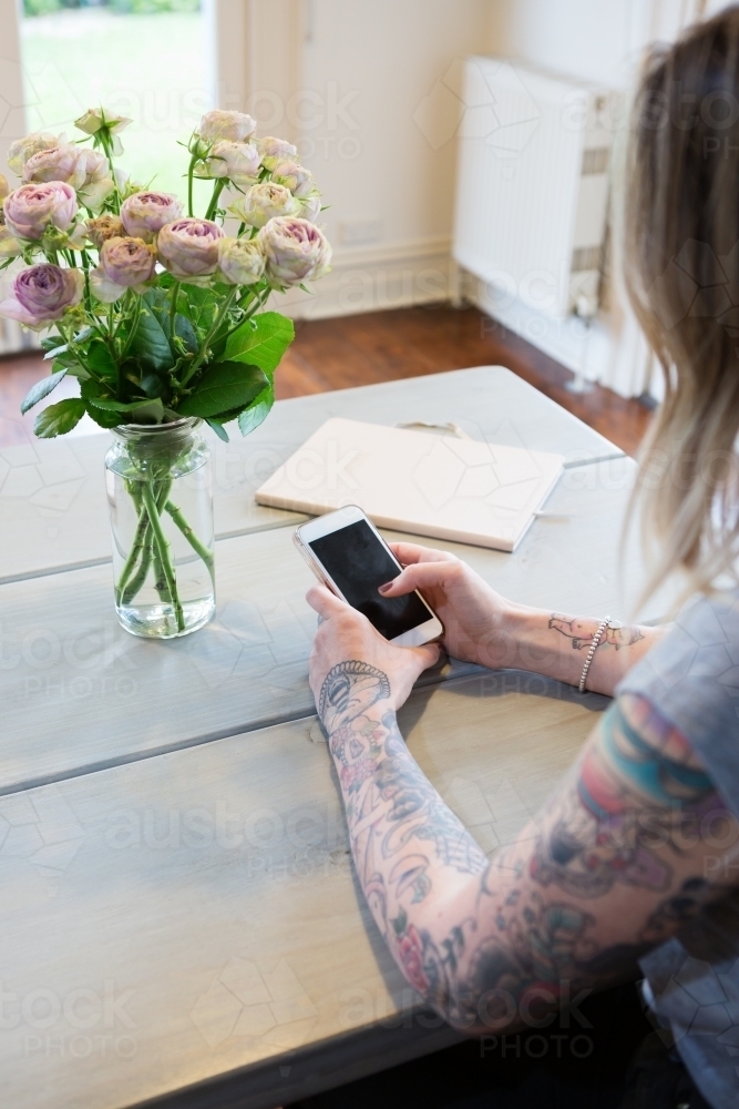 Gen Y with tattoos using a mobile phone at home - Australian Stock Image