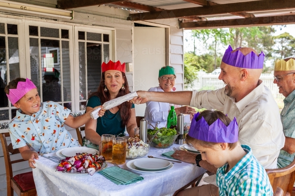 Generations of Australian family together at Christmas lunch table cracking crackers - Australian Stock Image