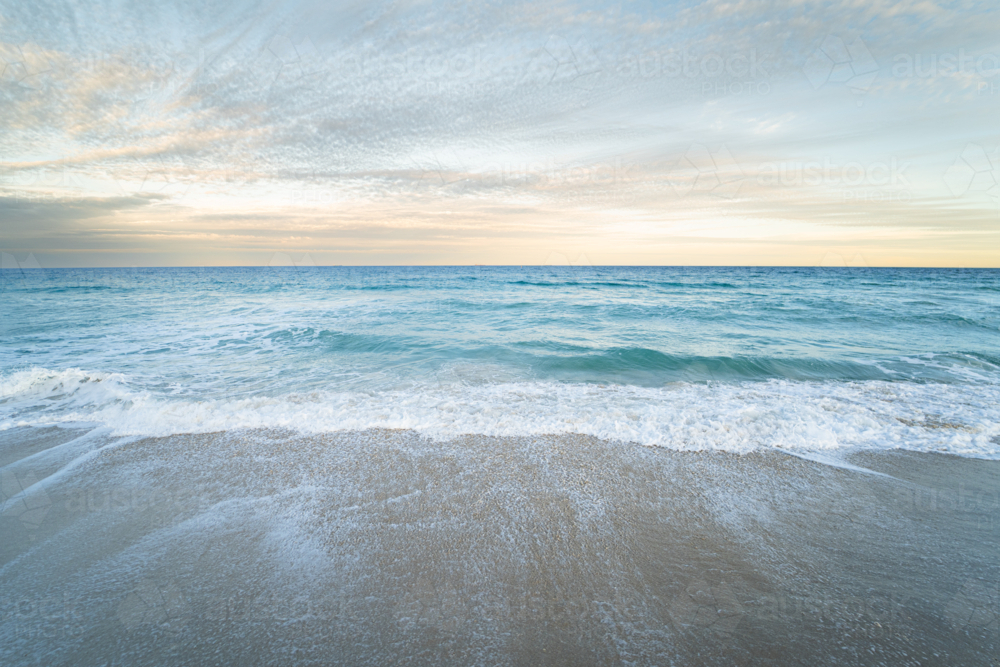 Gentle ocean tide washing over wet sandy beach at Scarborough Beach, Perth, Western Australia - Australian Stock Image