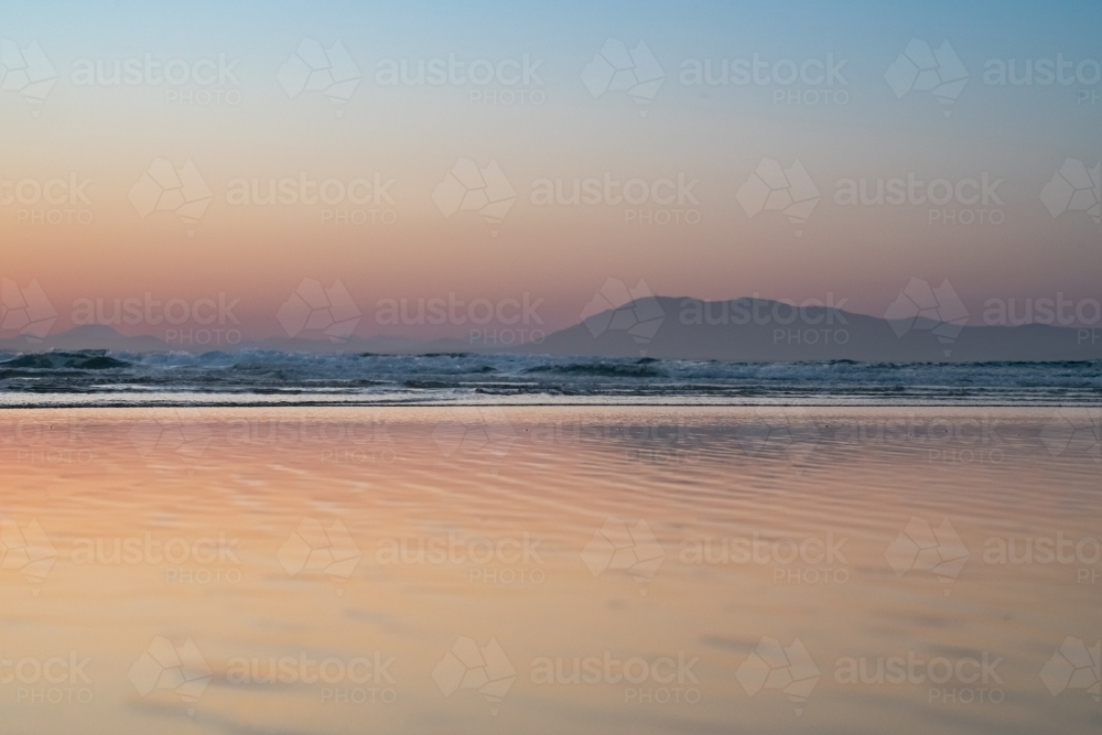 Gentle waves ripples on the surface of the ocean with a silhouette of a mountain range - Australian Stock Image