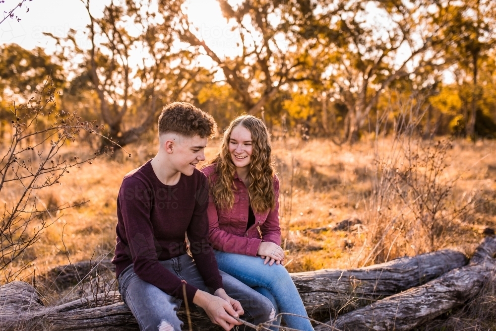 Girl and boy chatting and smiling in paddock at golden hour - Australian Stock Image