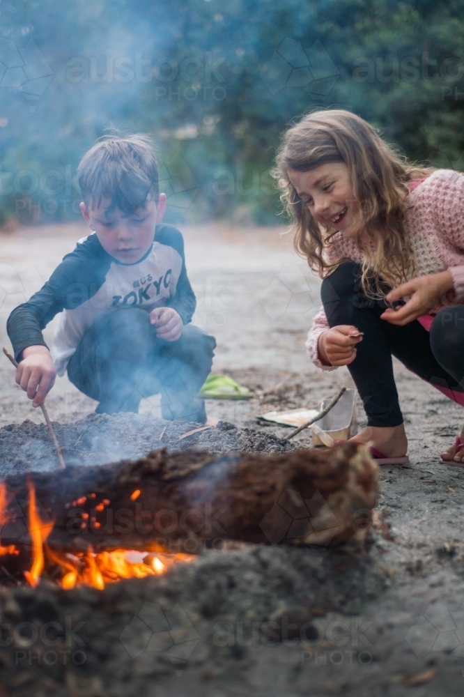 Girl and boy playing around a campfire in the bush - Australian Stock Image
