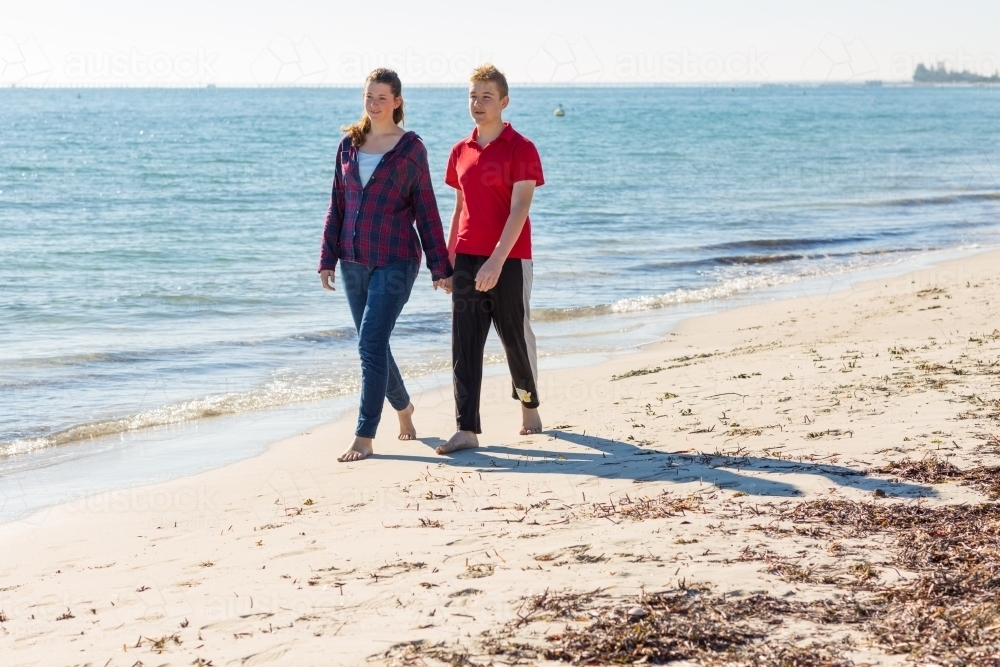 Girl and boy walking on beach holding hands - Australian Stock Image