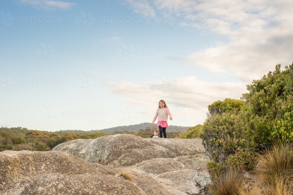 Girl and boy walking over boulder rocks - Australian Stock Image