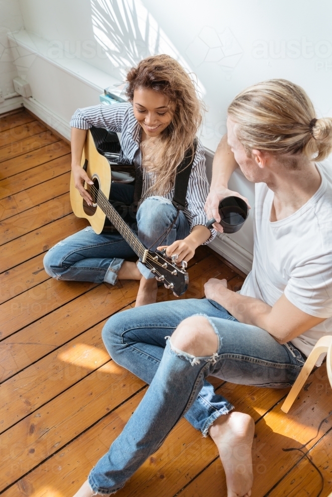 Girl and guy relaxing with a guitar on a wooden floor vertical - Australian Stock Image