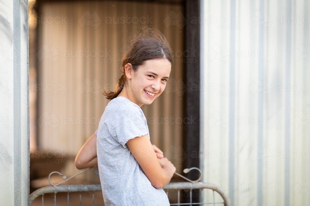 girl at gate looking bashfully at camera - Australian Stock Image