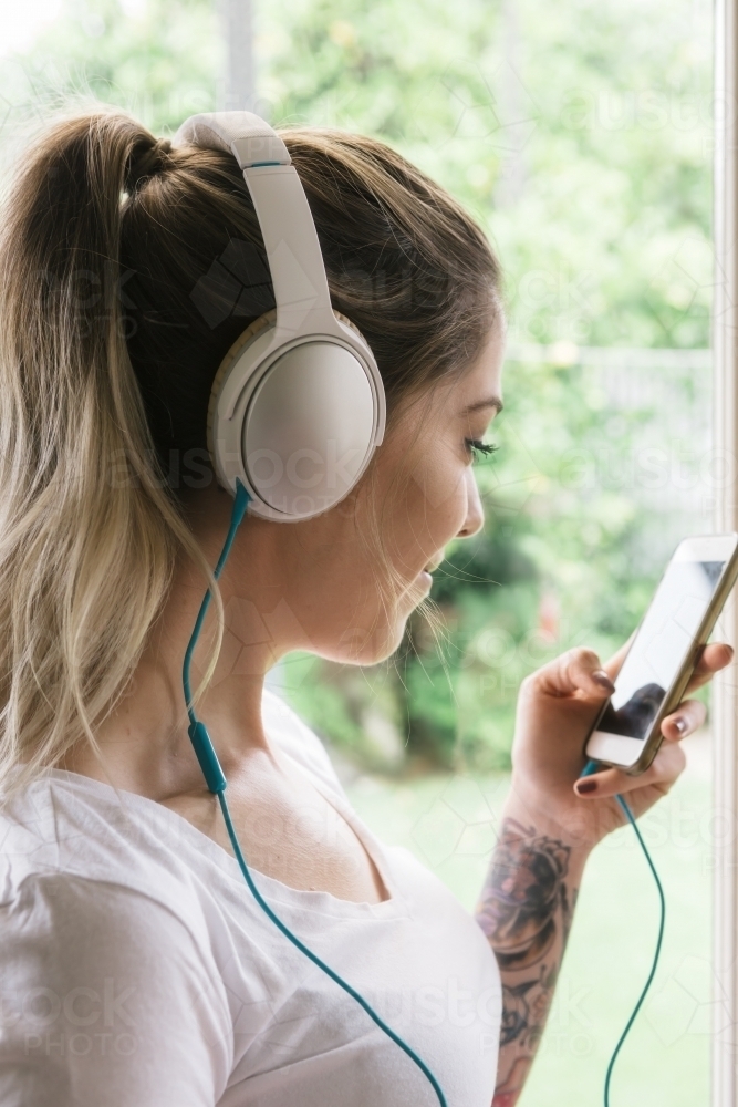 Girl at home listening choosing songs on her smartphone with headphones - Australian Stock Image