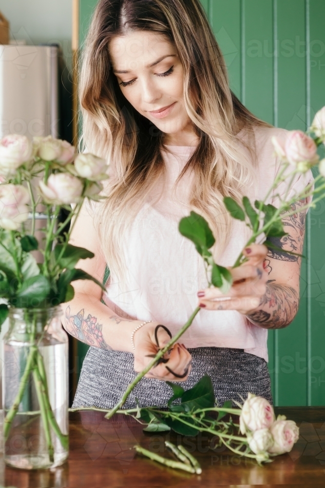 Girl at home trimming fresh pink roses and arranging in a vase - Australian Stock Image