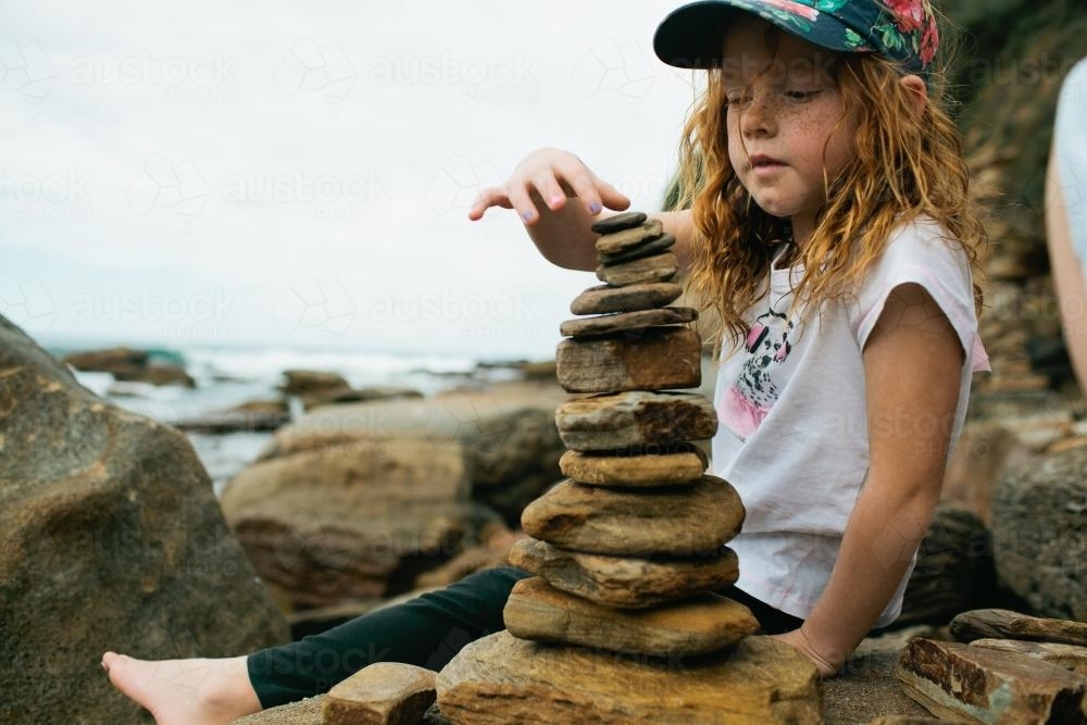 Girl balancing rocks at the beach - Australian Stock Image
