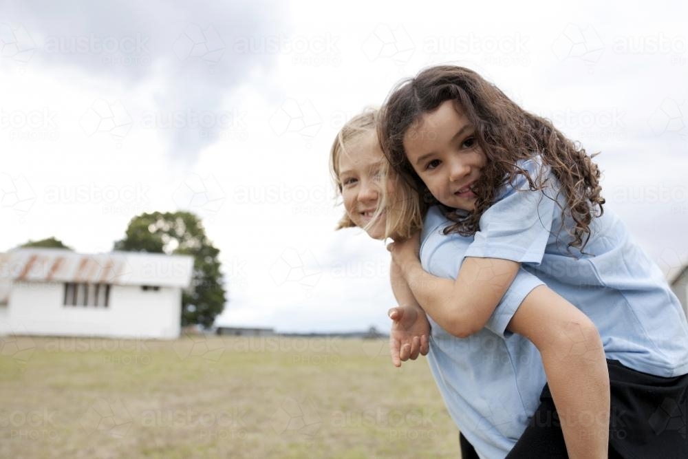 Girl carrying school friend on back on rural property - Australian Stock Image