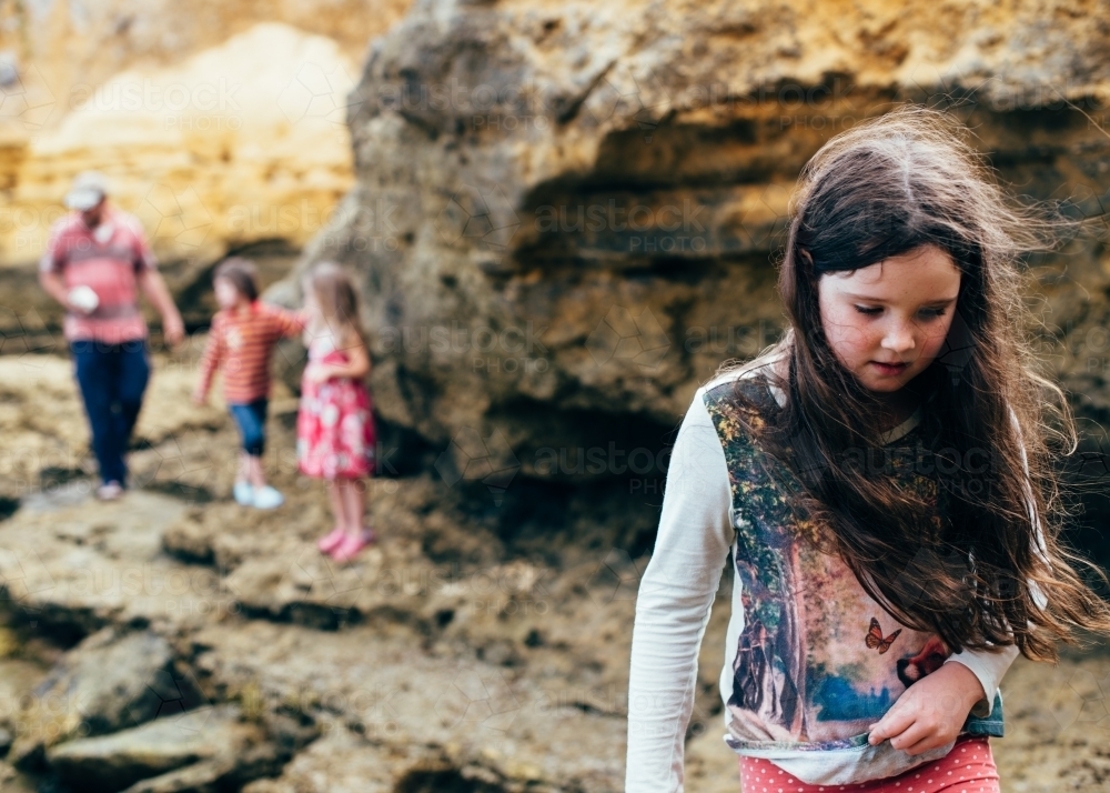 Girl carrying shells, family in background. Exploring limestone beach - Australian Stock Image