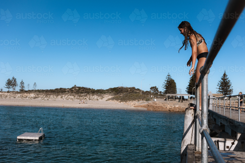 Girl climbing jetty rail to jump into the ocean in the golden summer sun - Australian Stock Image