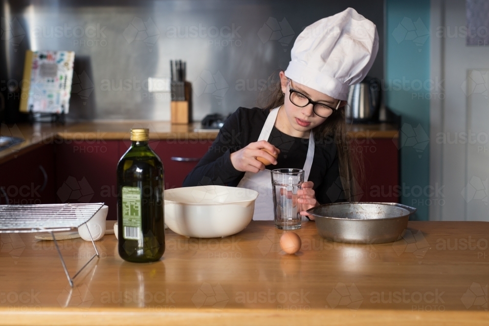 Girl cracking egg while baking a cake - Australian Stock Image