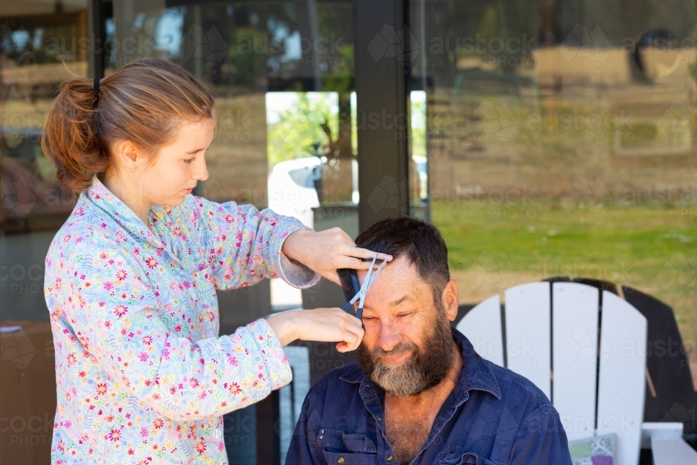 Girl cutting dad's hair on verandah at home - Australian Stock Image