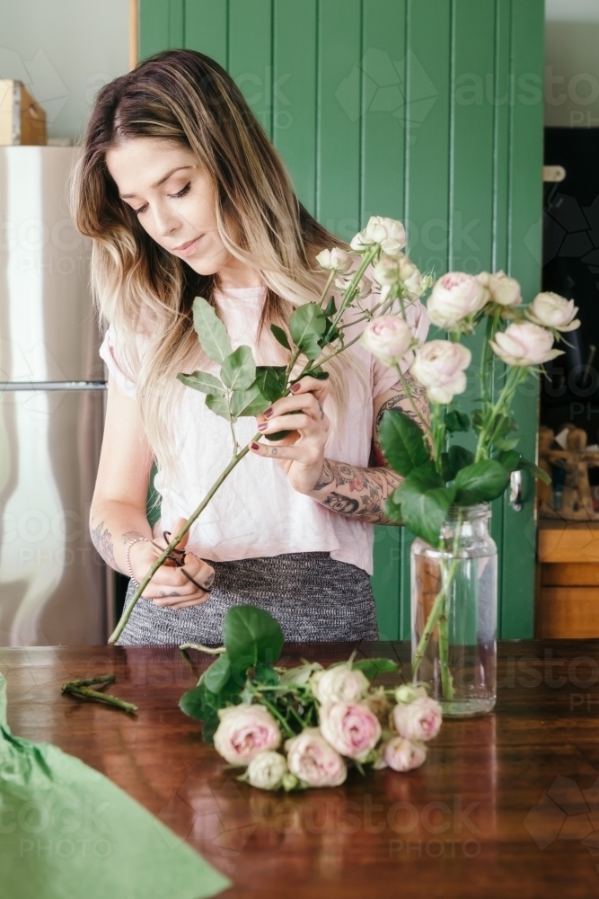 Girl cutting the stem of a pink rose in the kitchen - Australian Stock Image