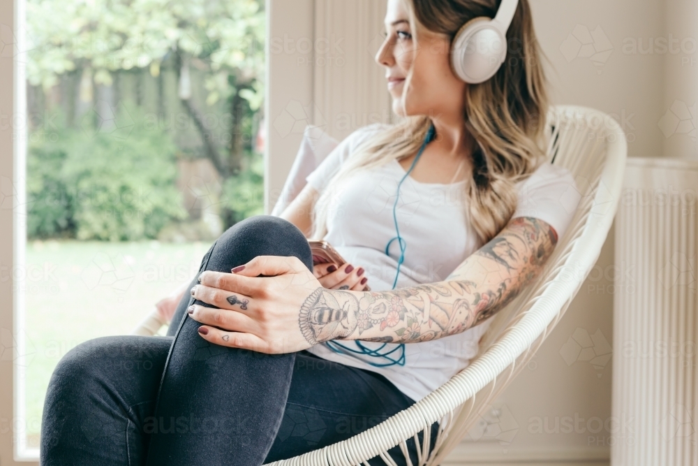 Girl daydreaming while listening to music in a relaxing chair - Australian Stock Image
