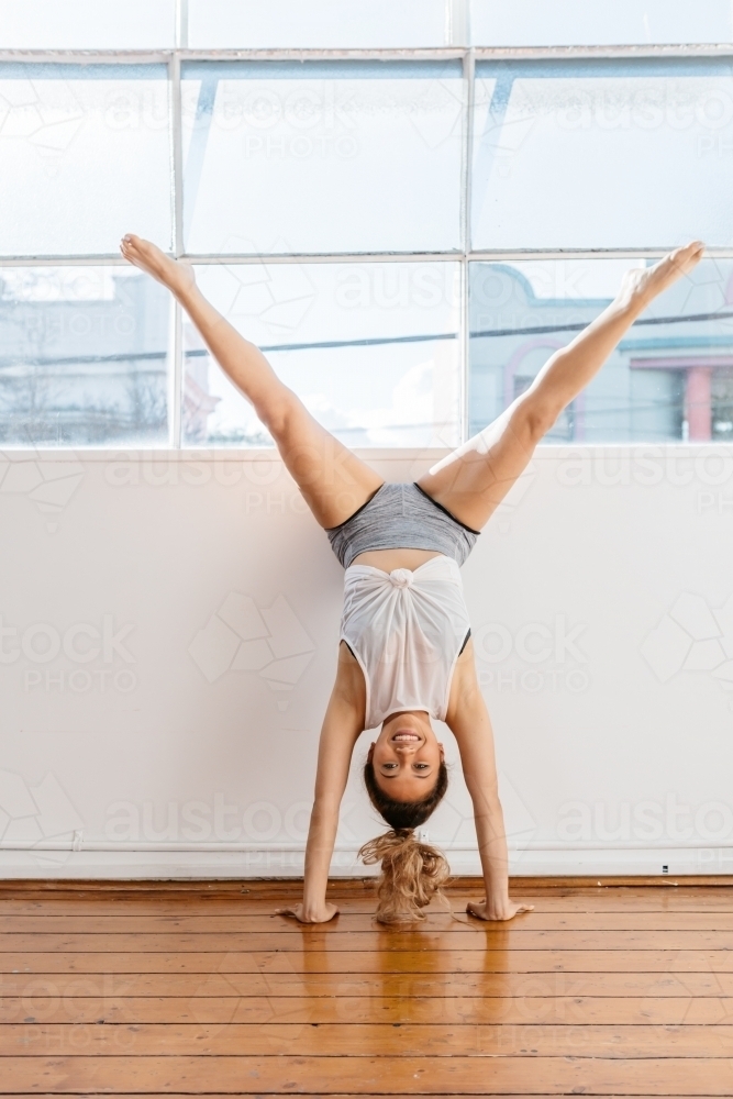 Girl doing a handstand and scissors pose in a dance studio - Australian Stock Image