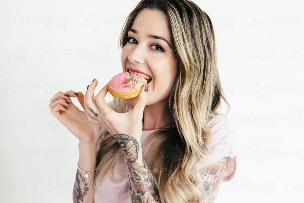 Girl eating a pink donut and looking at the camera laughing - Australian Stock Image