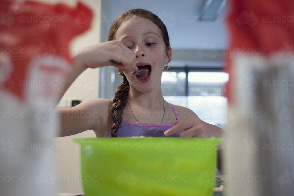 Girl eating from spoon while baking - Australian Stock Image