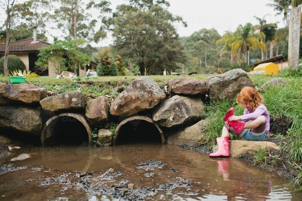 Girl exploring a stormwater drain in gumboots - Australian Stock Image
