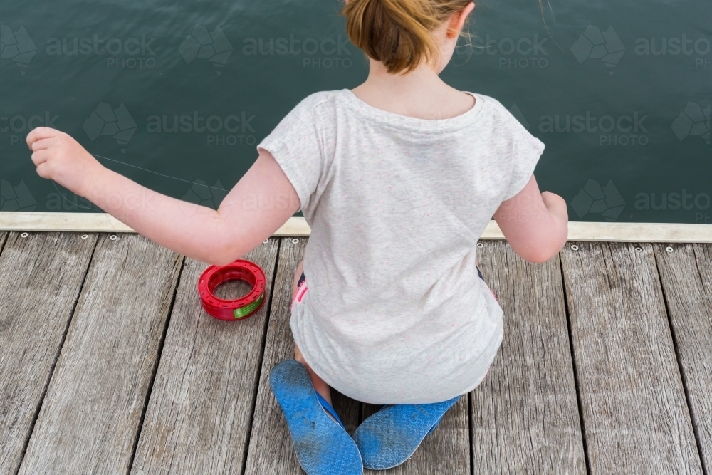 girl fishing with a hand reel from a wooden jetty - Australian Stock Image