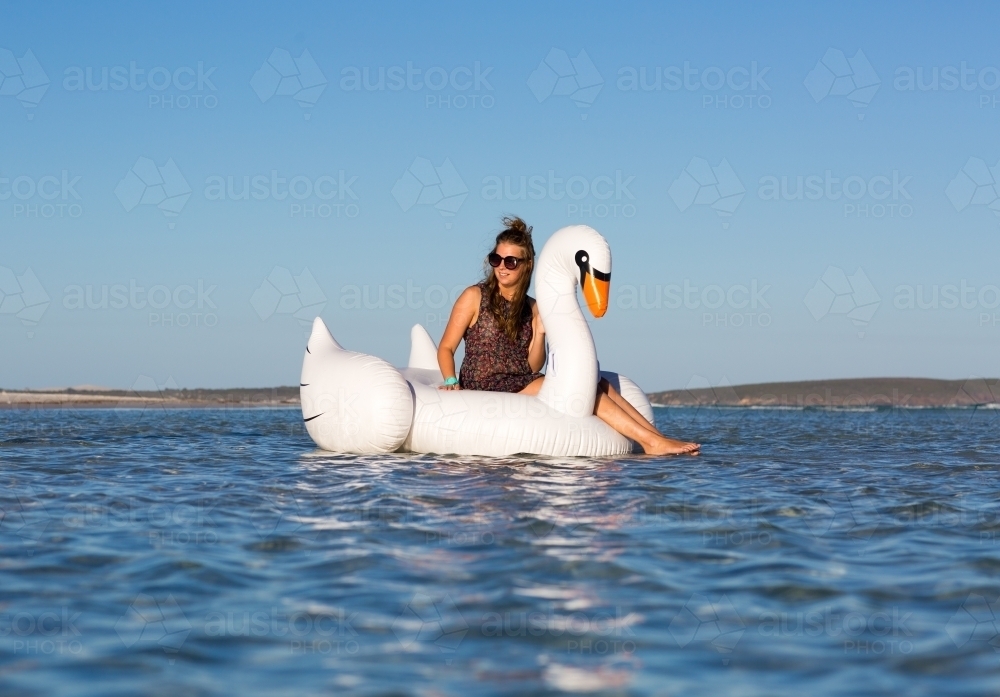 Girl floating on giant inflatable swan on lake - Australian Stock Image