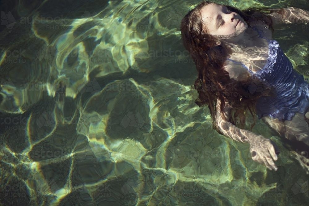 Girl floating on her back in sunlit water - Australian Stock Image